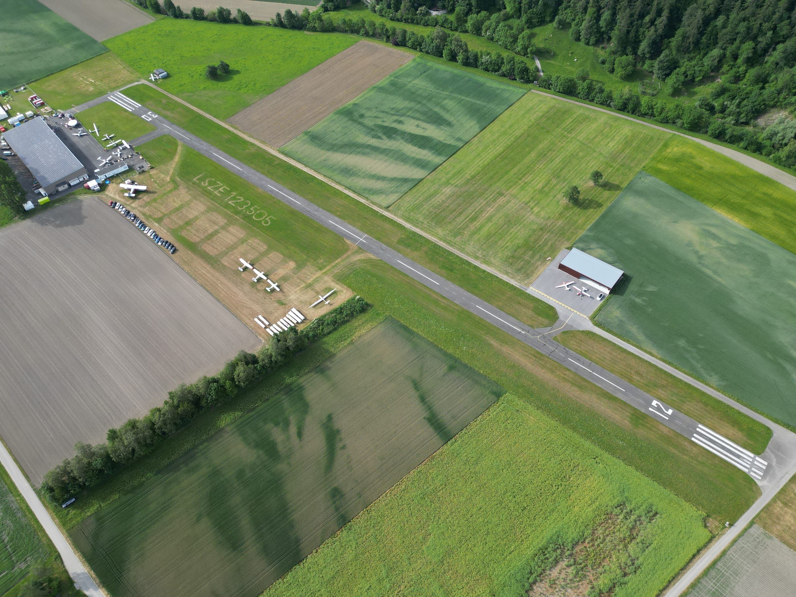 Bad Ragaz airfield from above: the runway between fields, the hangars and parked aircraft at the edge