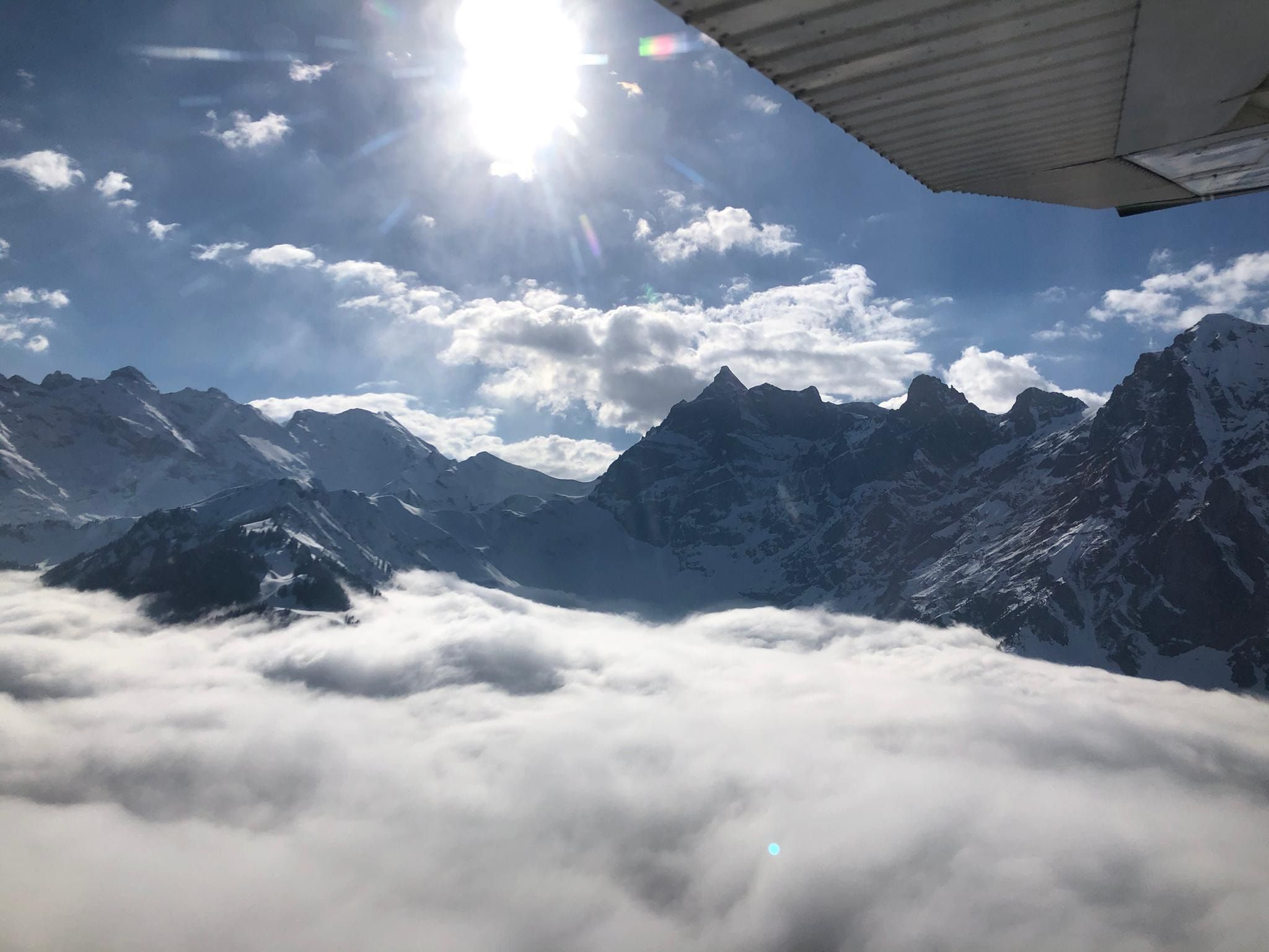 Above a sea of fog: snowy peaks rise from the clouds, the Cessna’s wing above